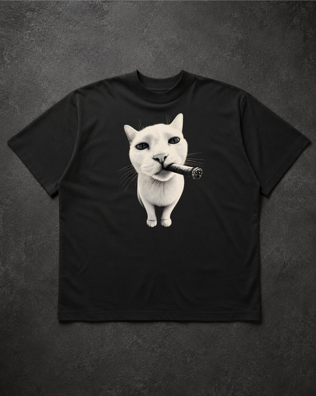 A black oversized t-shirt laid flat on a dark textured background, featuring a graphic print of a white cat with a cigarette in its mouth.