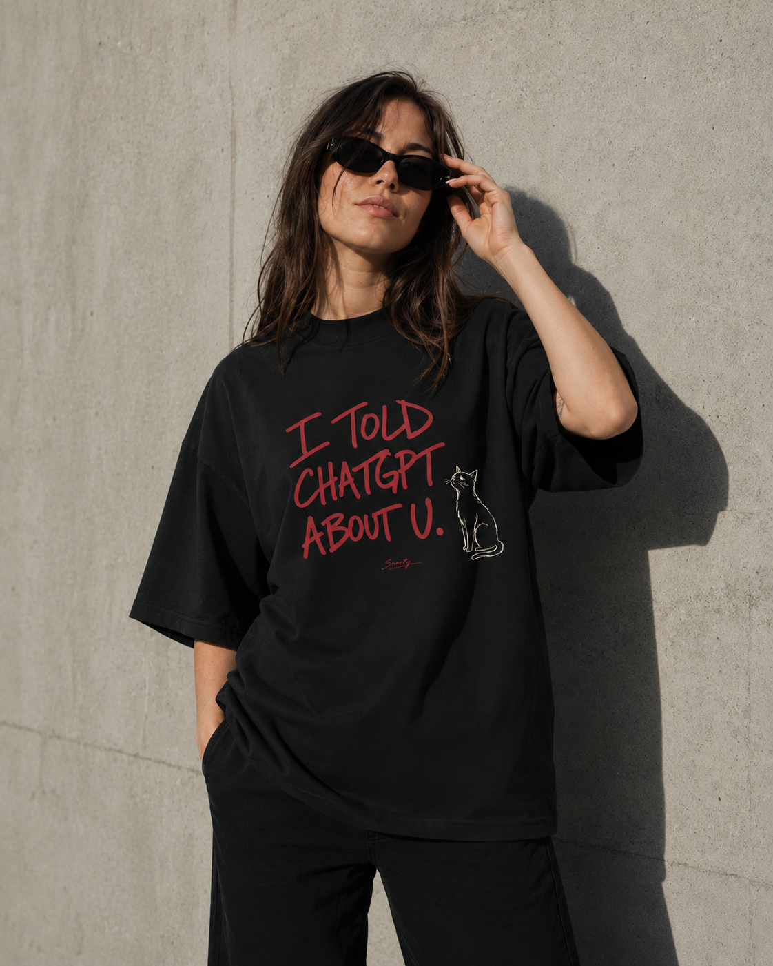 Person wearing a black t-shirt with text and a graphic, standing against a concrete wall.