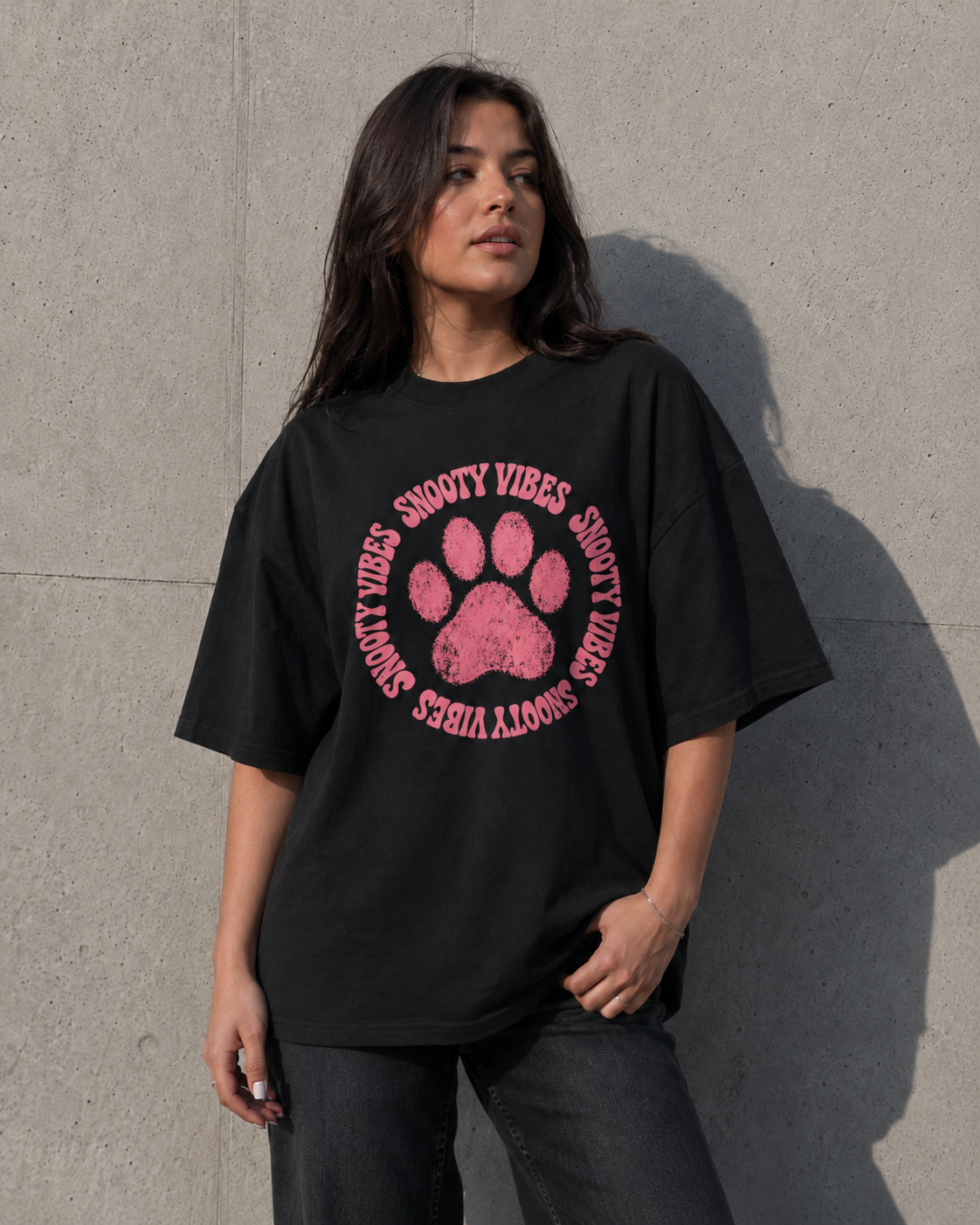 Person wearing a black t-shirt with pink paw print design and text against a concrete wall.