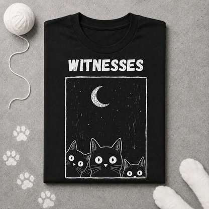 Black t-shirt with cat illustration and 'WITNESSES' text on a gray surface with paw prints.