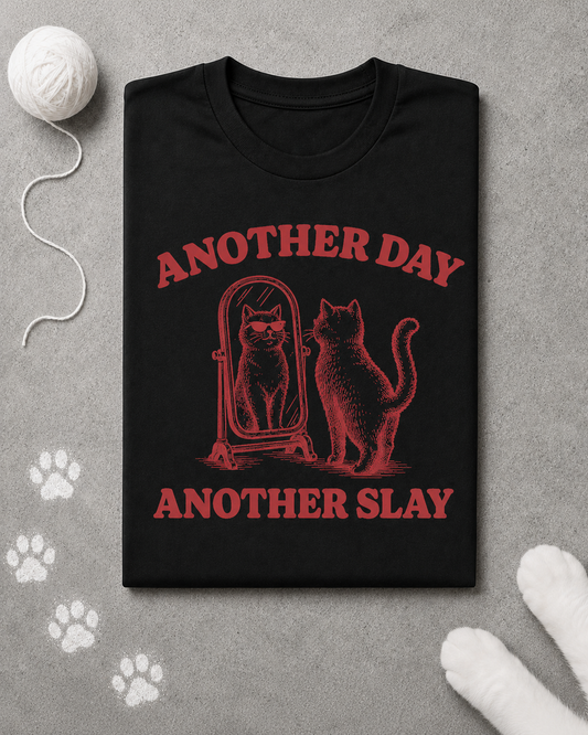 Black t-shirt with red graphic and text 'Another Day, Another Slay' on a gray surface with paw prints.