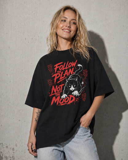 Person wearing a black t-shirt with a graphic design and text against a concrete wall.