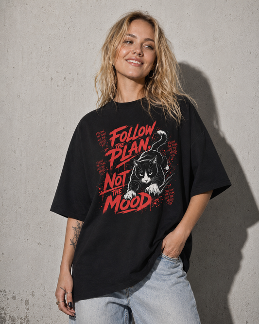 Person wearing a black t-shirt with a graphic design and text against a concrete wall.