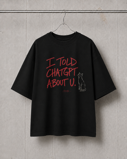 Black t-shirt with red text and a cat graphic on a hanger against a concrete wall.