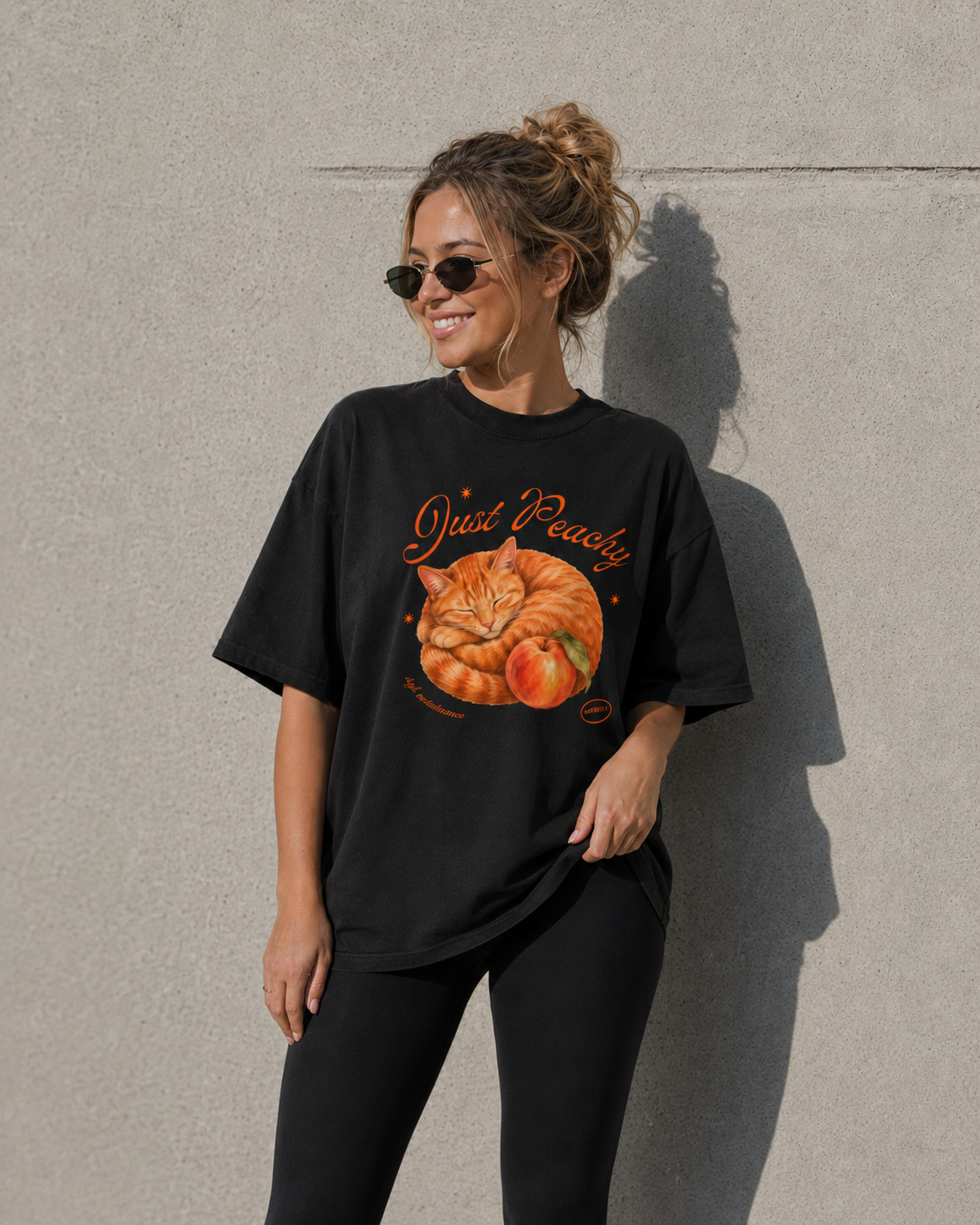 Woman wearing a black t-shirt with a pumpkin and cat graphic against a gray wall.
