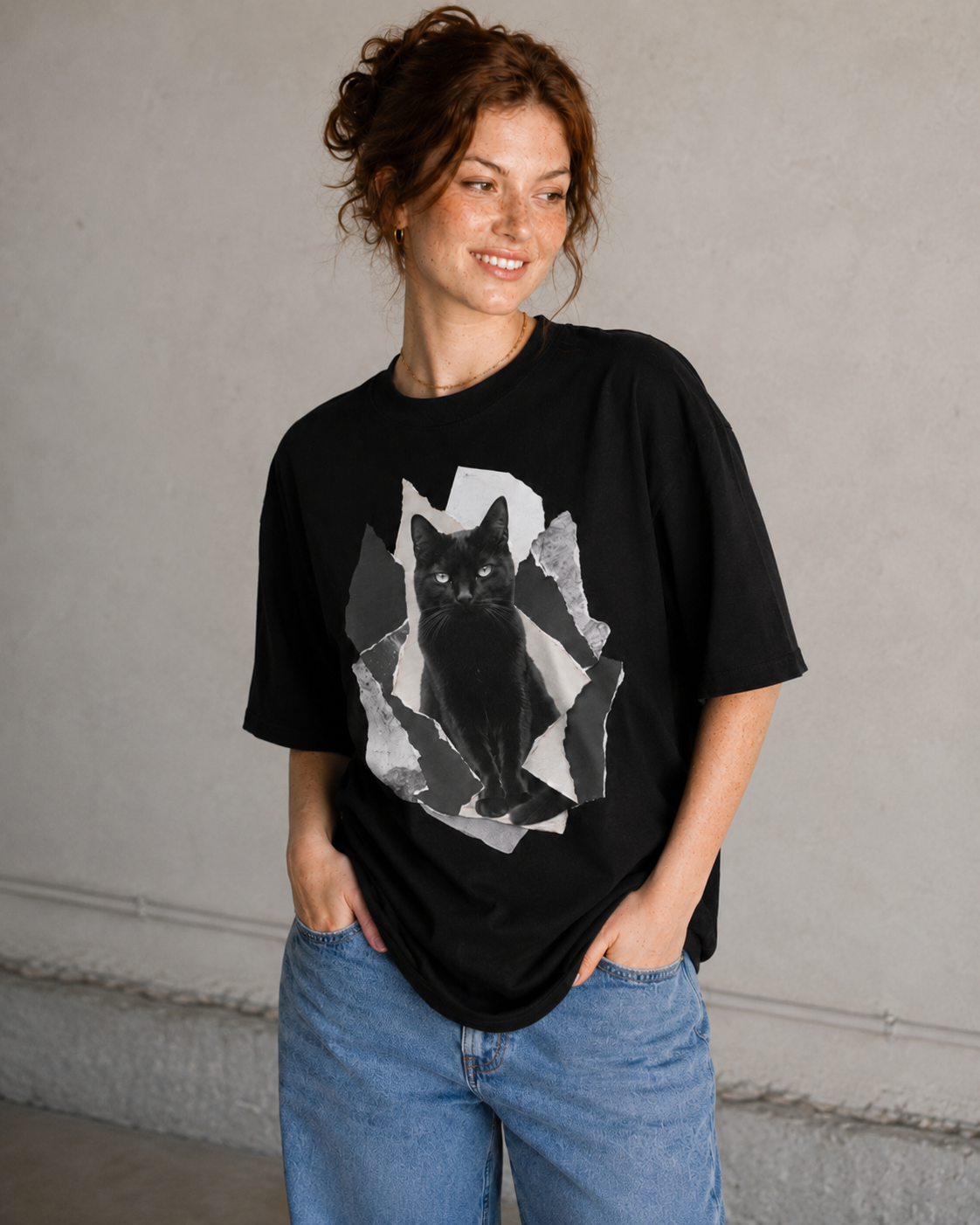 Woman wearing a black t-shirt with a graphic of a cat, standing against a plain wall.