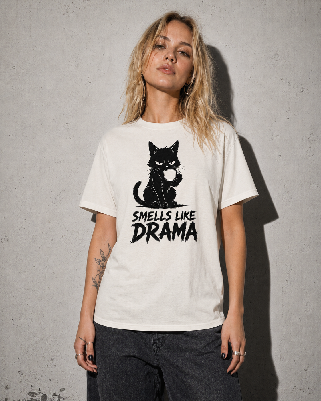 Person wearing a white t-shirt with a black cat graphic and text 'SMELLS LIKE DRAMA' against a gray background